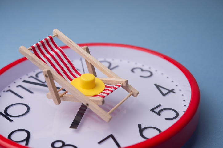 Red beach chair and hat on red clock with blue background. Annual leave travel period for relaxation, time to travel concept.