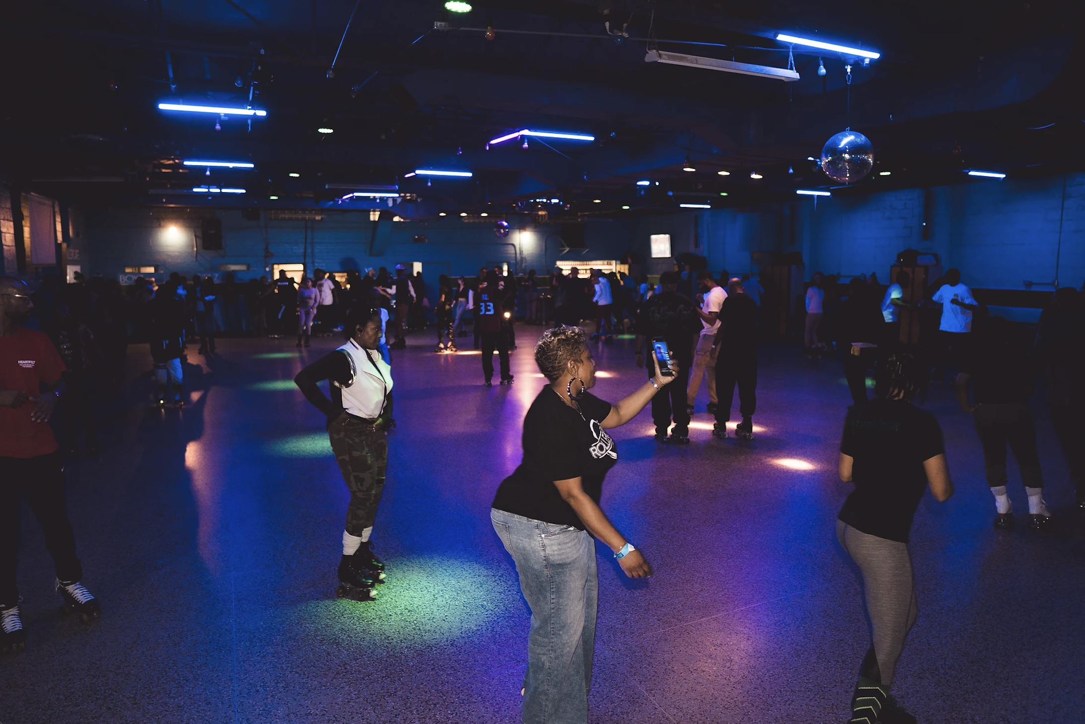 A crowded dance floor with people dancing under colorful neon lights and a disco ball.