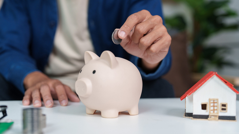 Person putting coin into piggy bank for home savings and financial goals.